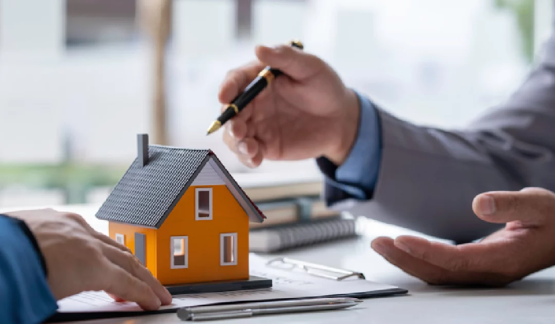 Two people discussing paperwork with a small house model on a desk, showing that a Title Company in Utah guiding home sellers through closing.